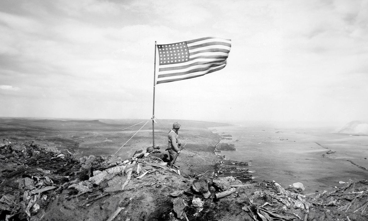 A member of the American military stands beside a US flag raised after the Battle of Iwo Jima.